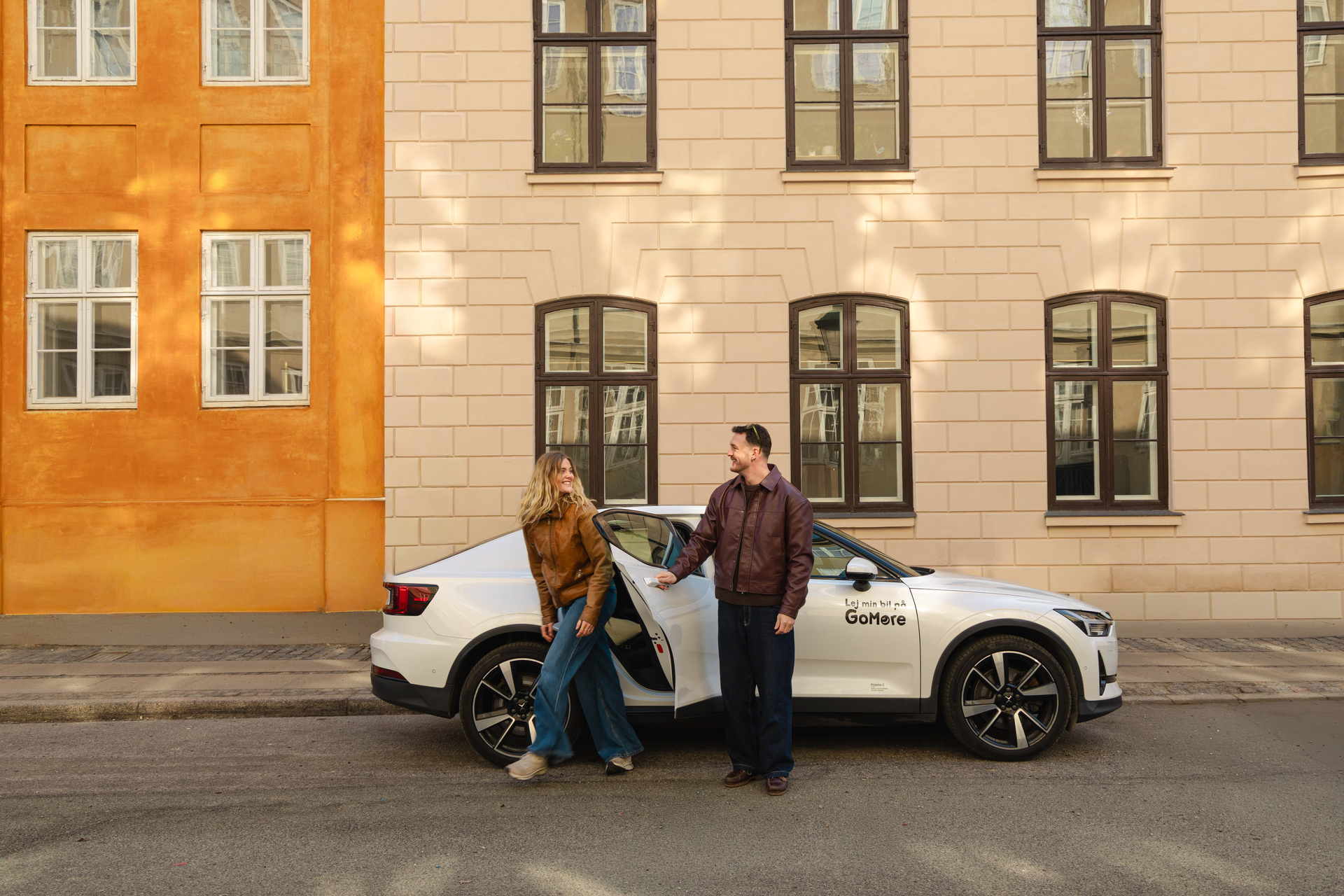 Two people beside a GoMore-branded shared car